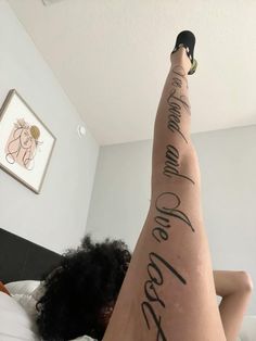 a woman laying on top of a bed with her legs up and writing on the leg