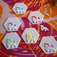 small cross stitch unicorns are arranged in rows on a colorful surface with flowers and leaves