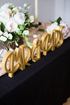 the table is set up with gold letters and flowers in vases on top of it