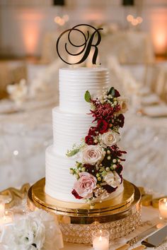 a three tiered wedding cake with red and white flowers on the top is surrounded by candles