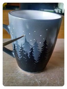 a coffee cup with trees painted on it and a pair of scissors in the middle