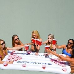 a group of women in bikinis holding cups and standing around an inflatable pool