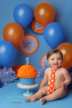 a baby wearing an orange and white tie sitting in front of blue backdrop with balloons