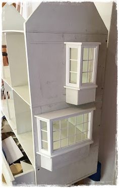 the doll house is made out of wood and has white trim on it's windows