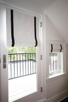 an open window with black and white blinds in a room next to a door that has a balcony on the other side