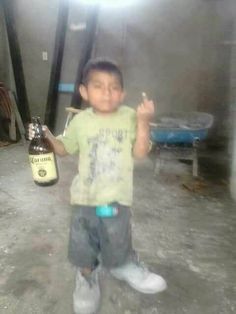 a young boy holding a beer bottle in his right hand and standing on the floor