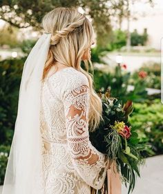 a woman in a wedding dress is holding a bouquet and looking at the camera with her back to the camera