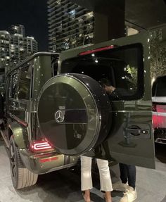 a man standing next to a green mercedes g - class suv with its door open