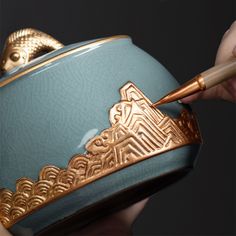 a person holding a blue and gold bowl with a brush in it