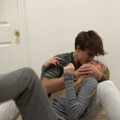 a man and woman sitting on the floor with their arms around each other as they kiss