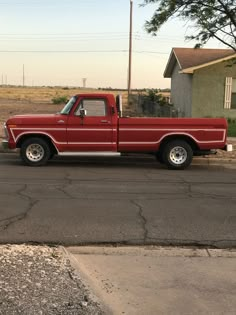 a red pick up truck parked on the side of the road in front of a house