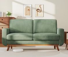 a green couch sitting in front of a wooden dresser next to a white wall with two paintings on it