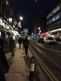 people walking down the street at night in an area with tall buildings and lots of lights