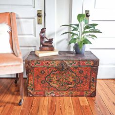 an old trunk is sitting on the floor next to a chair and potted plant