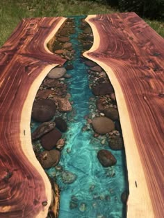 a long wooden table with blue water in the center and rocks on both sides, as well as green grass