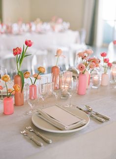 the table is set with pink and orange flowers in vases, candles, and plates