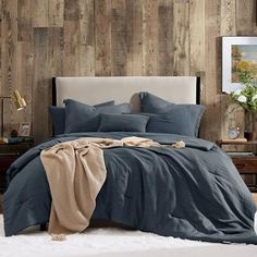 a bed with blue sheets and pillows in a room that has wood paneling on the walls