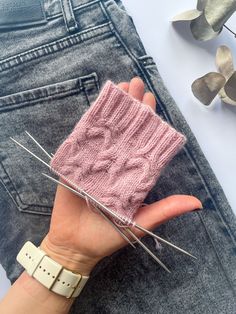 a woman's hand holding a pink knitted piece of clothing with pins sticking out of it