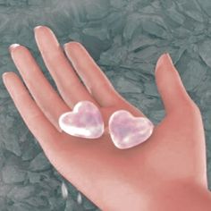 two pink hearts are placed on the palm of a person's hand, with water droplets surrounding them