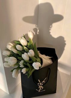 a bouquet of white tulips in a black paper bag with a shadow on the wall behind it