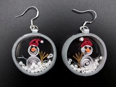 a pair of earrings that have been made to look like snowmen in a glass dome