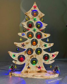 a wooden christmas tree with colorful ornaments on it's sides and lights around the base