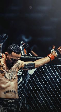 a man with tattoos on his arms and chest standing in front of a metal fence