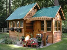 a small wooden cabin in the middle of a field with flowers and trees around it