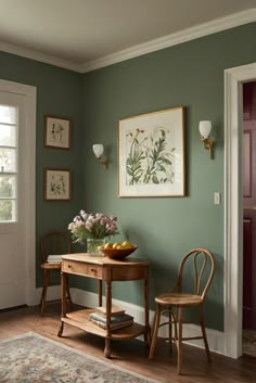 two chairs and a table in a room with paintings on the wall behind them,