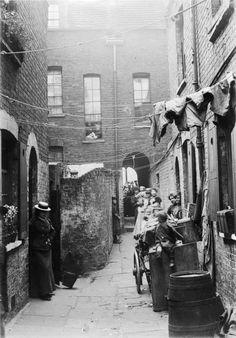 an old black and white photo of people on bicycles in the alleyway between two buildings