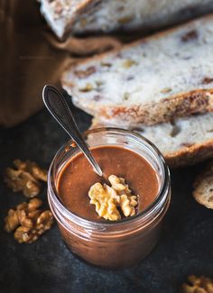 a jar filled with peanut butter next to sliced bread and walnuts on a table