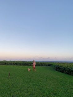 a man standing on top of a lush green field next to a small white dog