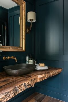 a bathroom with blue walls and wood counter top, gold framed mirror above the sink