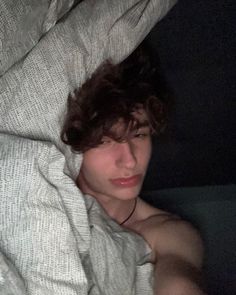 a young man laying in bed under a blanket