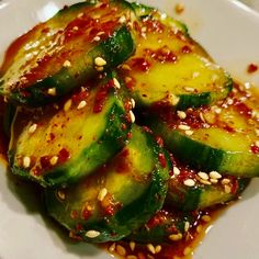 a white plate topped with sliced cucumbers covered in marinara sauce and sesame seeds