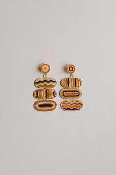 two pairs of earrings with designs on them sitting on a white surface in front of a wall