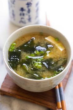 a white bowl filled with soup next to chopsticks on top of a wooden board