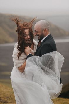 a man in a suit and woman in a wedding dress on the side of a hill