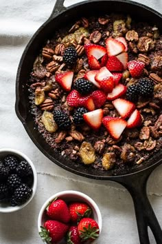 a skillet filled with fruit and nuts on top of a white cloth next to bowls of berries