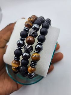 This unique set is the perfect Father's Day gift, combining three powerful stones known for their protective and grounding properties. Each bracelet is meticulously handcrafted, offering a stylish and versatile accessory that enhances any outfit, from casual to formal. The Black Onyx beads provide a sleek, matte finish that exudes elegance and strength. The Tiger's Eye beads add a touch of warmth and sophistication with their rich, golden hues, symbolizing courage and confidence. The Hematite beads, with their metallic luster, bring a modern and bold touch, known for their grounding and balancing energies. This bracelet set is strung on a durable elastic cord, ensuring a comfortable and secure fit for all wrist sizes. Whether worn individually or stacked together, these bracelets make a po Stones Meanings, Male Bracelets, Masculine Jewelry, Swift Bracelets, Hematite Jewelry, Mens Bracelets, Lava Stone Bracelet, Birthday Flyer, Metallic Luster