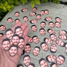 a hand is holding up a bunch of stickers with faces on them in the shape of men's heads