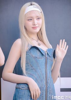 a young woman with long blonde hair wearing a denim dress and holding her hand up in the air