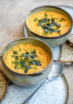 two bowls of soup on a plate with bread and silver spoons next to it