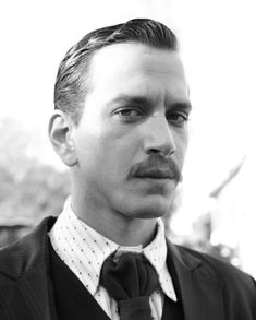 a man wearing a suit and tie with a moustache on his face is looking at the camera