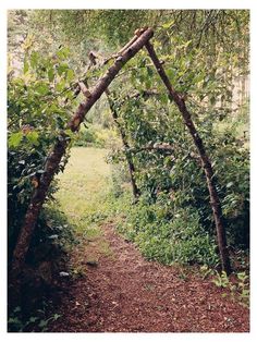 a wooden arch made out of branches in the middle of a garden with grass and trees