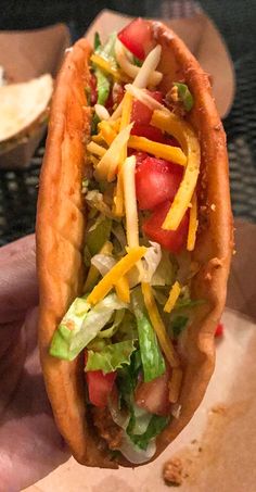 a hand holding a hot dog with cheese, lettuce and tomatoes