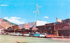 an old photo of cars parked on the side of the road in front of buildings