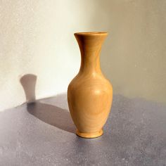 a wooden vase sitting on top of a table next to a shadow from the wall