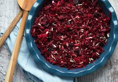 a blue bowl filled with beets and sunflower seeds next to a wooden spoon