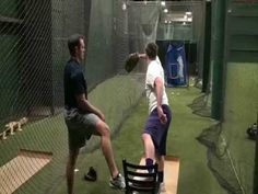 two men in batting cages playing baseball with one man on the bench and another standing up